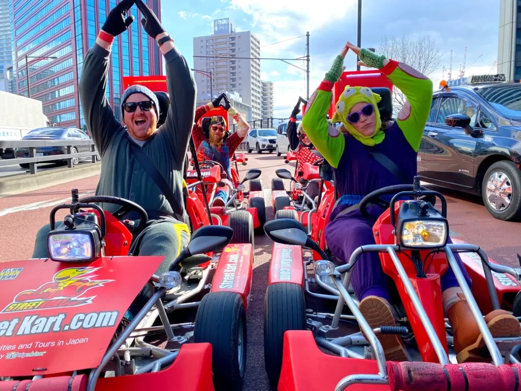 IMG_1502 - StreetKart Friends in red go-karts on a sunny city street, arms raised in celebration.