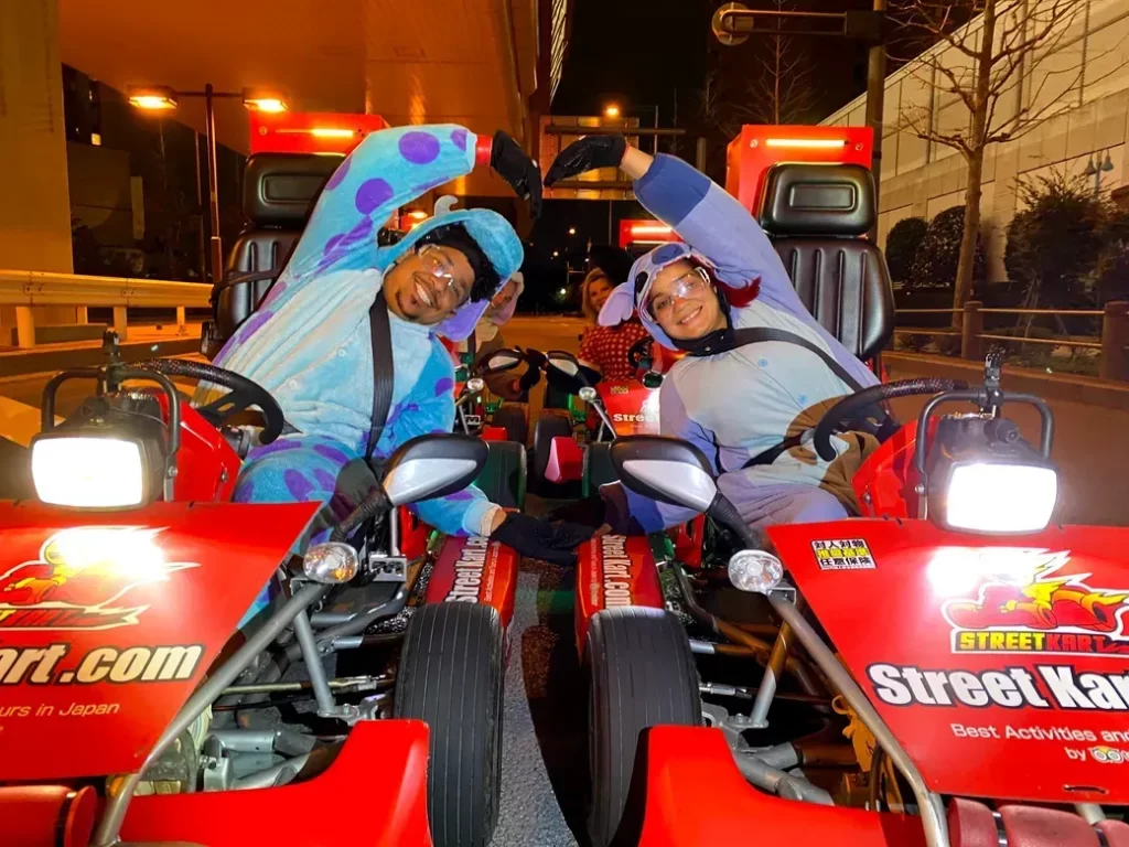 IMG_4272 - StreetKart Two people in colorful onesies on red go-karts at night, forming a heart shape with their arms between the karts.